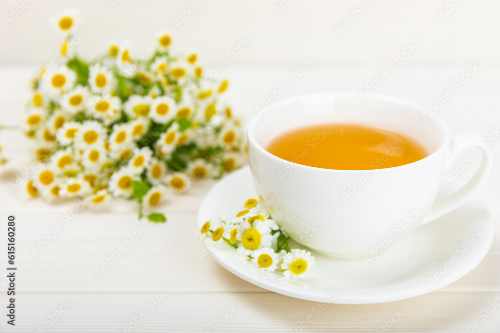 Chamomile herbal tea in a cup on a white wooden table with a bouquet of chamomile. Close-up. Copy space. Useful herbal drinks, immunity tea. Natural healer concept.Place for text. Chamomile herbal tea in a cup on a white wooden table with a bouquet of chamomile. Close-up. Copy space. Useful herbal drinks, immunity tea. Natural healer concept.Place for text.