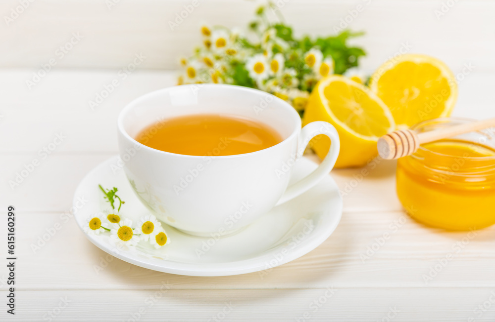 Herbal chamomile tea in a white cup on a white wooden table with honey, lemon and chamomile bouquet. Close-up. Copy space. Useful herbal drinks, immunity tea. Natural healer concept. Herbal chamomile tea in a white cup on a white wooden table with honey, lemon and chamomile bouquet. Close-up. Copy space. Useful herbal drinks, immunity tea. Natural healer concept.