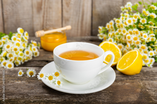 Herbal chamomile tea in a cup on a brown wooden table with honey, lemon and chamomile bouquet. Close-up. Copy space. healthy herbal drinks, immunity tea. Natural healer concept.Place for text.