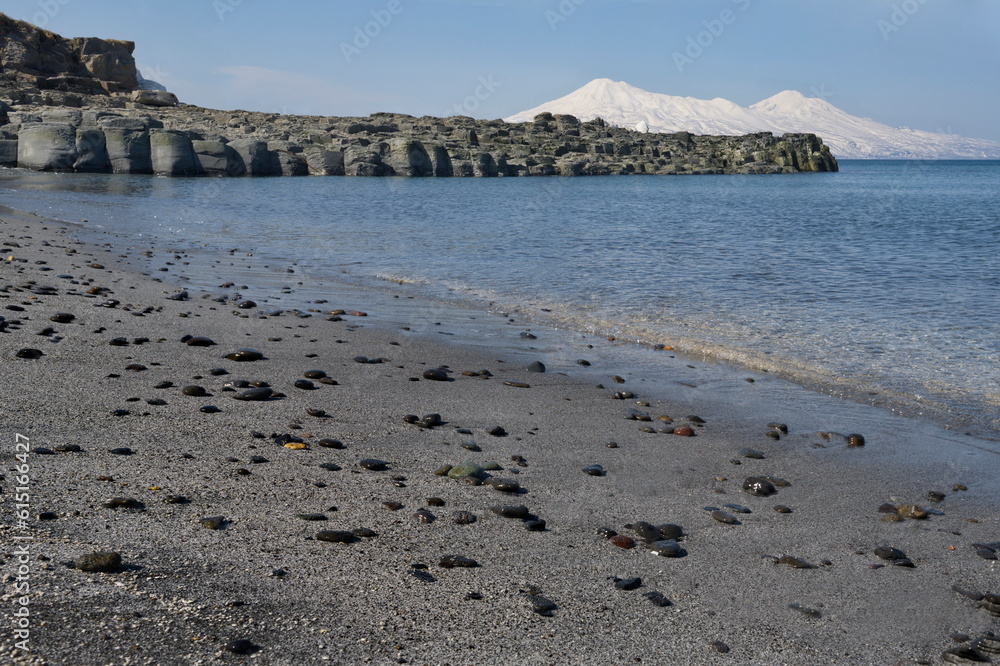 Russia. Far East, Kuril Islands. View of the Okhotsk coast of Iturup island with ash sand of volcanic origin against the background of two snow-covered volcanoes Chirip and Bogdan Khmelnitsky.