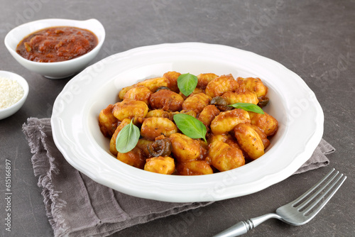 Traditional Italian potato gnocchi with tomato sauce, fresh basil and parmesan cheese on brown background.