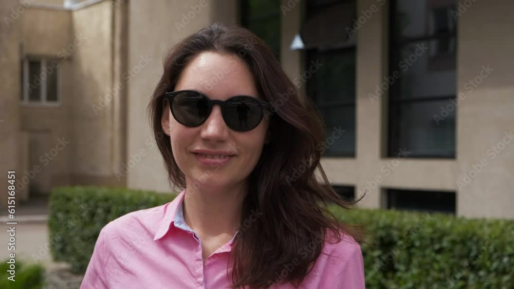 An attractive woman in sunglasses, spin around herself against the background of a modern business center building and looks into the camera Her hair rises up and flutters An attractive woman in sunglasses, spin around herself against the background of a modern business center building and looks into the camera Her hair rises up and flutters