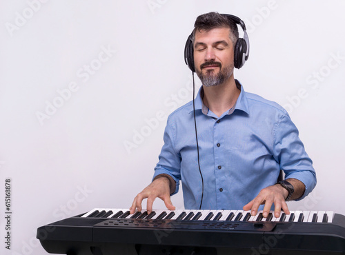 Smiling man with headphones playing keyboard piano enjoying music looking excited and happy, music record concept, art of composition