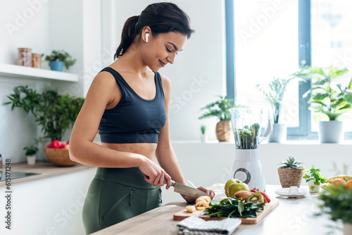 Obraz na plátně Shoot of athletic woman cutting fruits and vegetables to prepare a smoothie whil