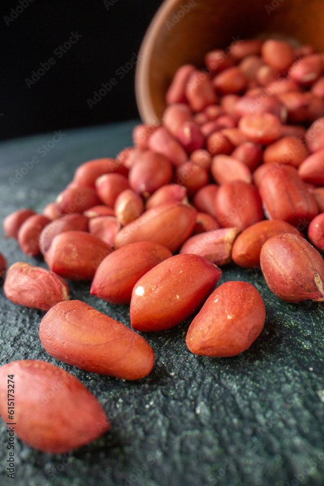 Close shot of red peanuts fallen from brown pot on blue and black background