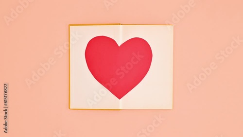 Yellow vintage book appear and open on pastel orange background. Heart in open book. Stop motion