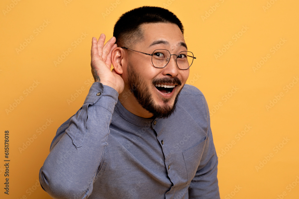Curious Cheerful Asian Man Holding Hand Near Ear, Trying To Overhear Something Curious Cheerful Asian Man Holding Hand Near Ear, Trying To Overhear Something