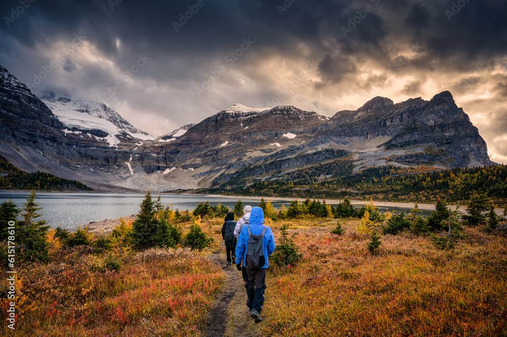 Group of traveler trekking on meadow with moody sky over mount Assiniboine in autumn forest at national park