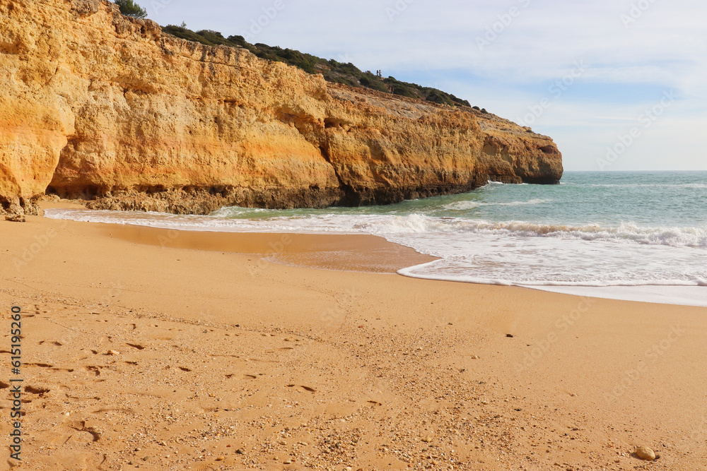 Sandy beach next to the Atlantic Ocean and a limestone cliff on a sunny winter day on the Seven Hanging Valleys Trail in southern Portugal.