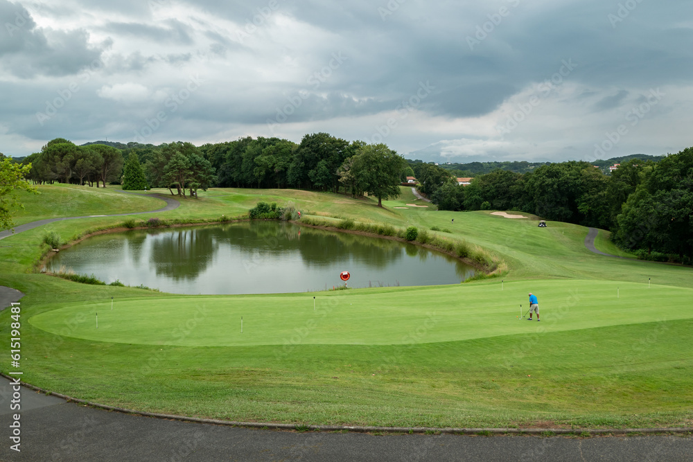 Golfista junto ao lago ao fundo a dar a tacada na bola num dia muito nublado