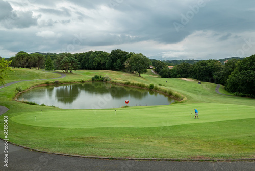Golfista junto ao lago ao fundo a dar a tacada na bola num dia muito nublado