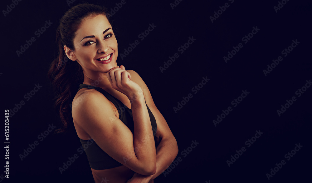 Confident sport woman in sport bra smiling and looking in camera, fitness trainer standing front view, workout in gym on studio black background with empty copy space. Closeup