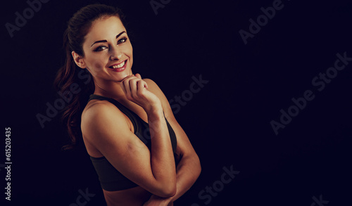 Confident sport woman in sport bra smiling and looking in camera, fitness trainer standing front view, workout in gym on studio black background with empty copy space. Closeup © nastia1983