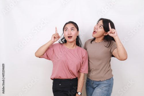 Wow expression of two asian women standing while pointing above. Isolated on white