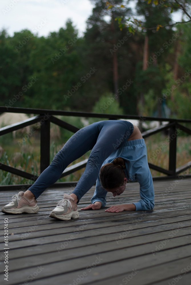 © Veronica Holubnycha - Girl in blue gym suit is doing exercises in the park in cloudy rainy weather.