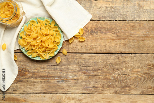 Plate with raw conchiglie pasta on wooden background