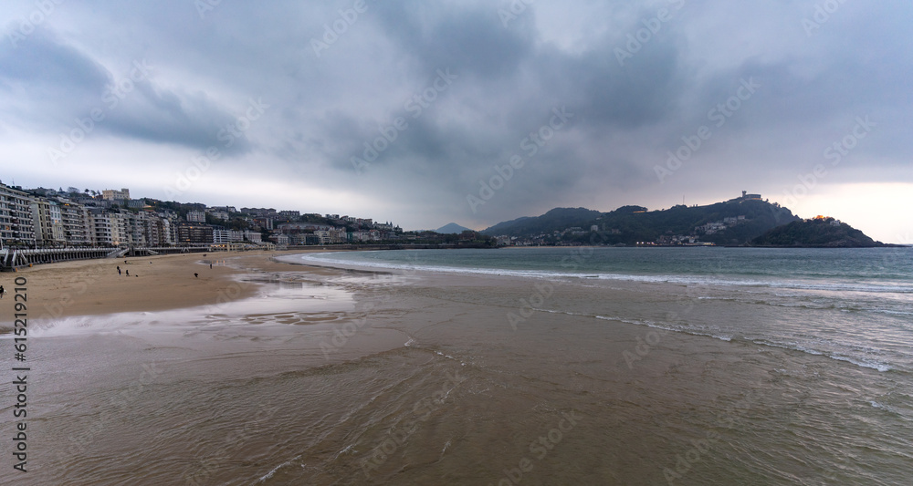 La Concha beach in San Sebastian with Mount Igueldo in the background. People walking on the sand La Concha beach in San Sebastian with Mount Igueldo in the background. People walking on the sand