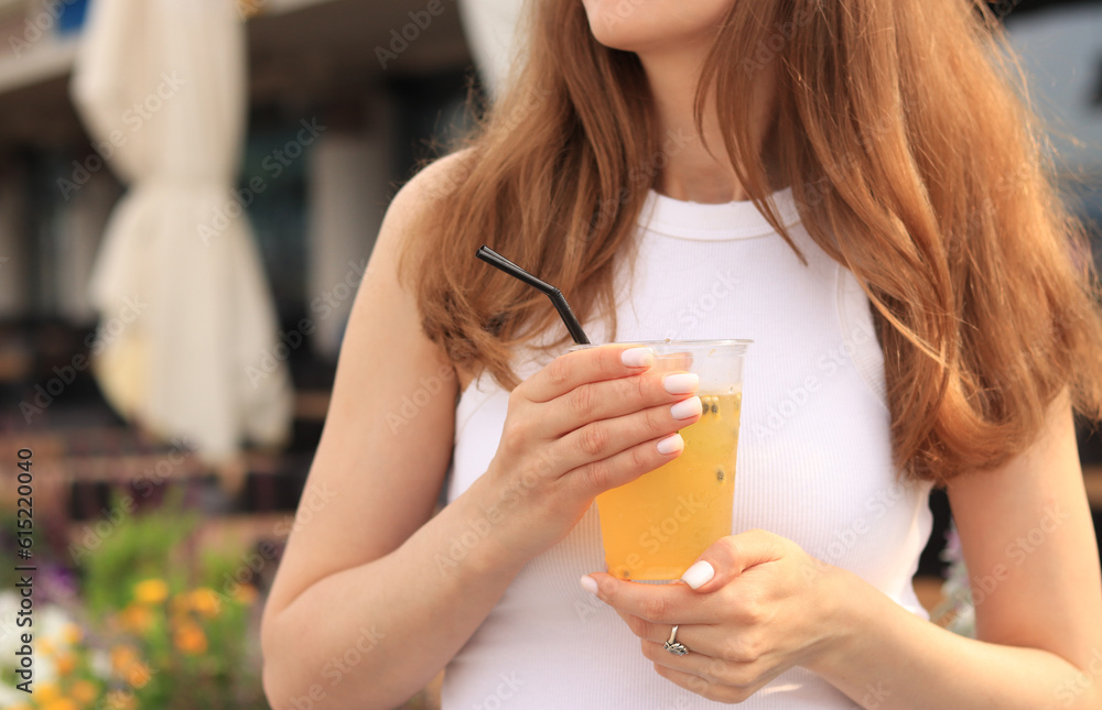 Passion fruit lemonade. Summer drink in the hands of a girl. Takeaway lemonade. Cold lemonade with ice in a female hand against a summer street cafe Passion fruit lemonade. Summer drink in the hands of a girl. Takeaway lemonade. Cold lemonade with ice in a female hand against a summer street cafe