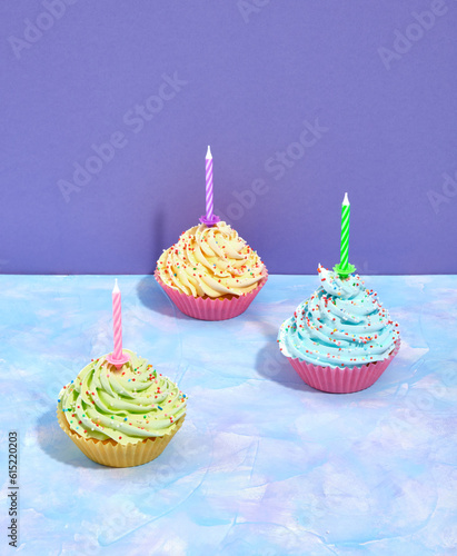 Yummy, luxury, sweets cupcakes with yellow, blue and green cream. Colored sprinkles and a celebration candles. photo