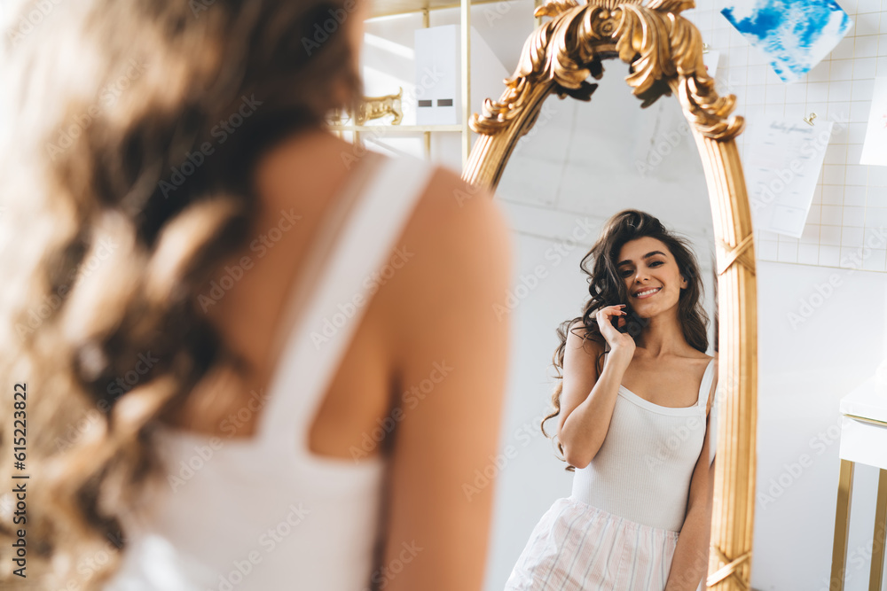 Naklejka premium Happy young lady in sleepwear looking in mirror at home