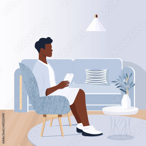 Vector illustration in a flat style and light colors. A young black man in a stylish summer t-shirt and shorts sits in a comfortable chair in a modern interior and looks at the phone screen.