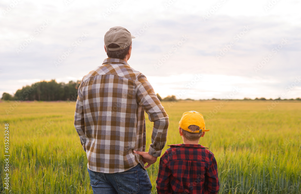 Farmer and his son in front of a sunset agricultural landscape. Man and a boy in a countryside field. Fatherhood, country life, farming and country lifestyle concept. Farmer and his son in front of a sunset agricultural landscape. Man and a boy in a countryside field. Fatherhood, country life, farming and country lifestyle concept.