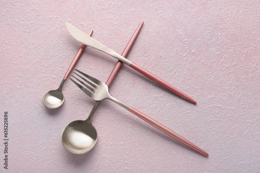 Stainless steel cutlery with pink handles on lilac background Stainless steel cutlery with pink handles on lilac background