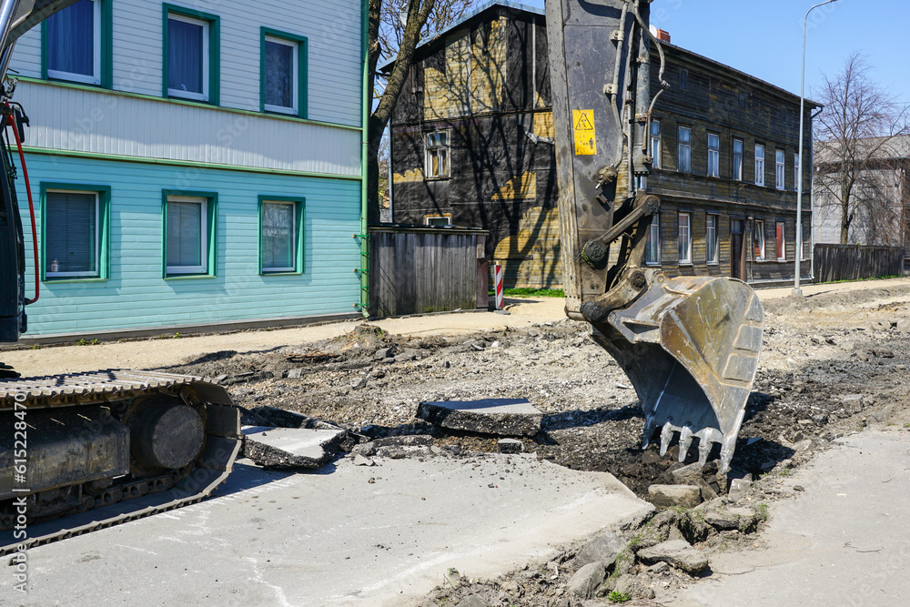 Fototapeta premium Crawler excavator with a bucket dismantle the asphalt before the reconstruction of the street