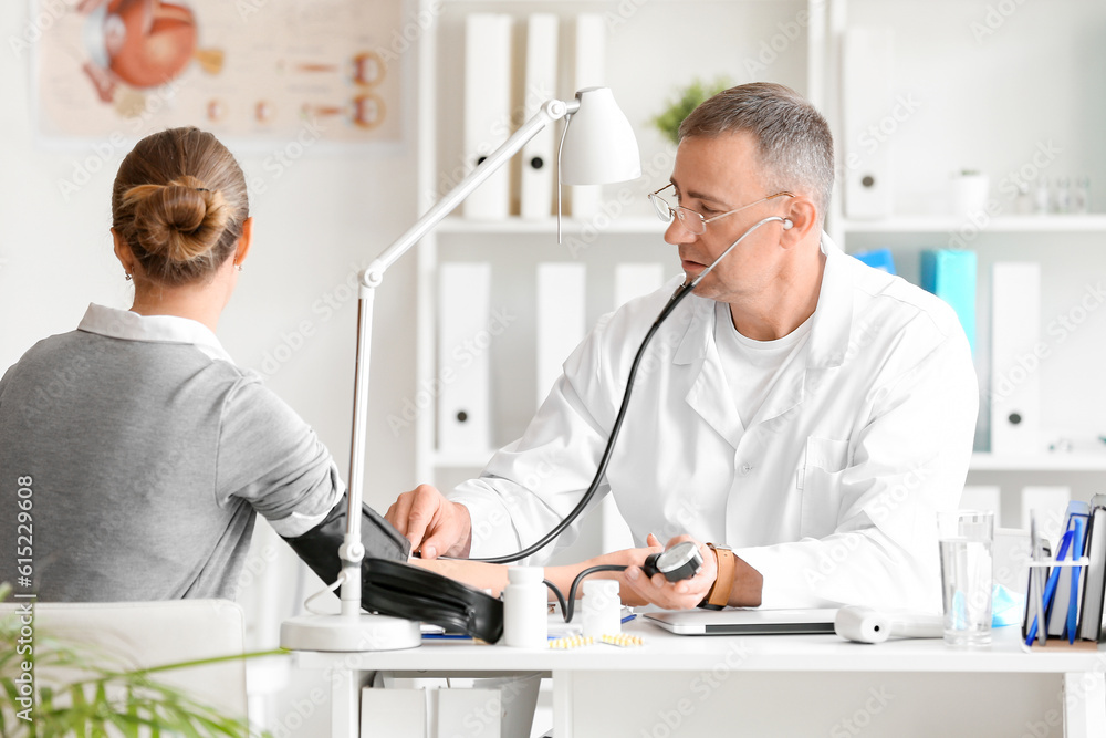 Mature male doctor measuring blood pressure of patient in clinic