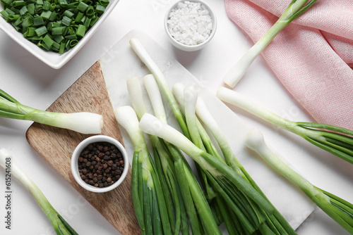 Board with fresh green onion and bowl of slices on white background