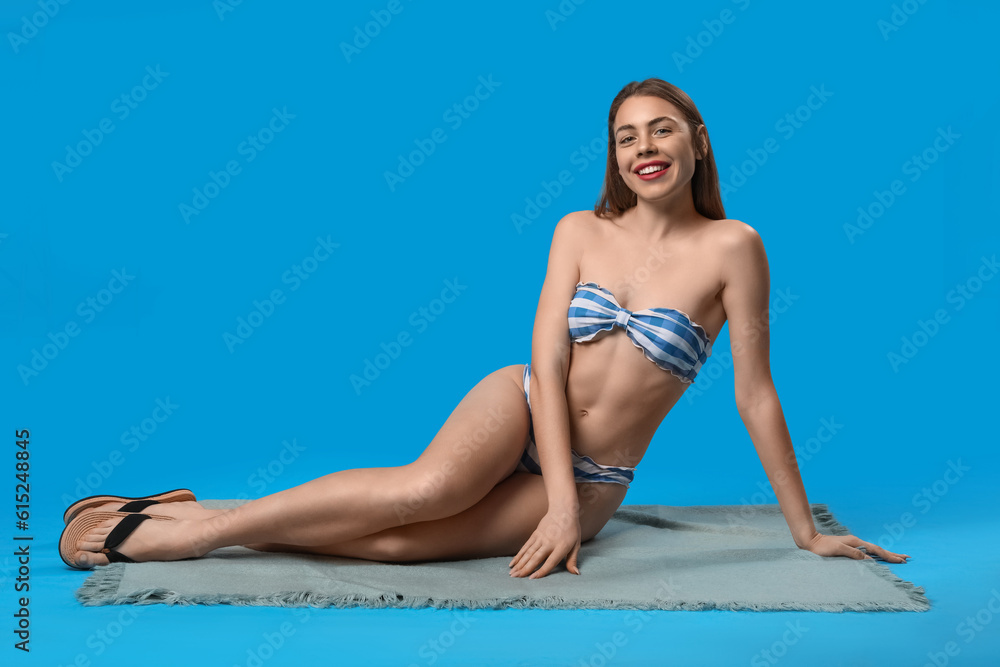 Young woman in swimsuit sitting on blue background