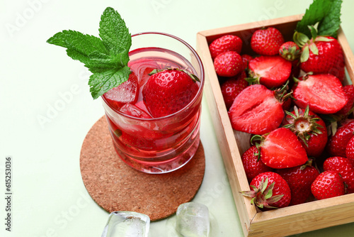 Glass of infused water and wooden box with strawberries and on green background