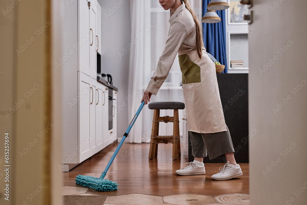Side view of young woman mopping floors and cleaning apartment on weekend, copy space