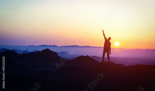 Man silhouette stand on peak of moutain with hand up. Success and motivation. Mountains landscape with sunset