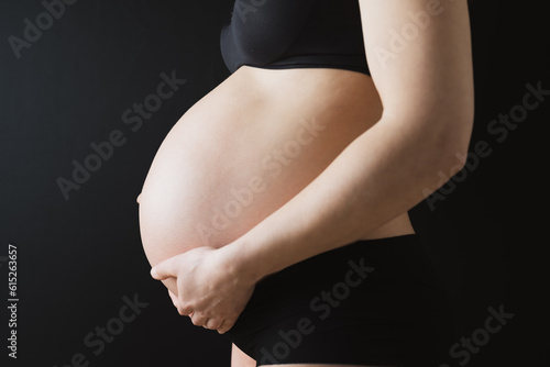 Side view of naked round belly of pregnant woman in underwear during last pregnancy month. Last month of pregnancy - week 36. Cropped. Black background. photo