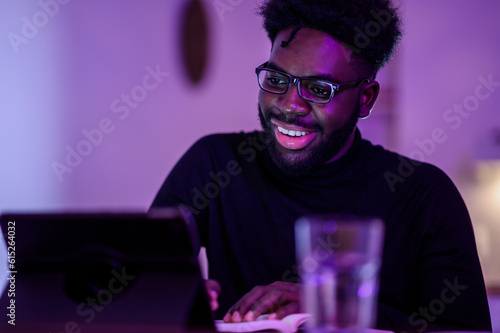 Portrait of a happy interracial man sitting at home and following a webinar on a tablet late at night.