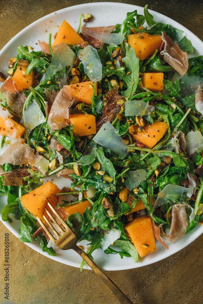 arugula salad with cheese, cantaloupe, prosciutto, pistachios on white