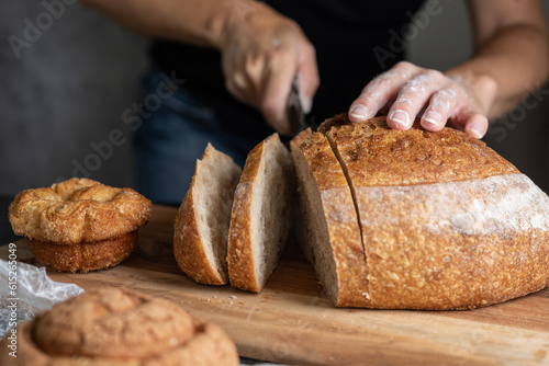 Fototapeta person cutting a loaf of bread on the table, space for text, focus on the bread