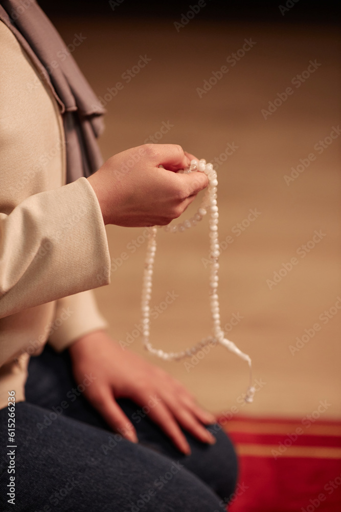 Obraz premium Close-up of hand of young Islamic woman with white rosary standign on her knees in front of camera at home and praying in silence
