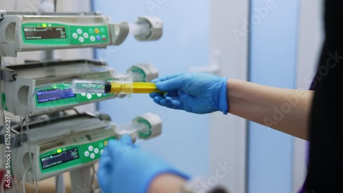 Gloved hands holding the syringe and pushing its forcer. Medic puts the syringe attached to a wire on infusion pump machine. photo