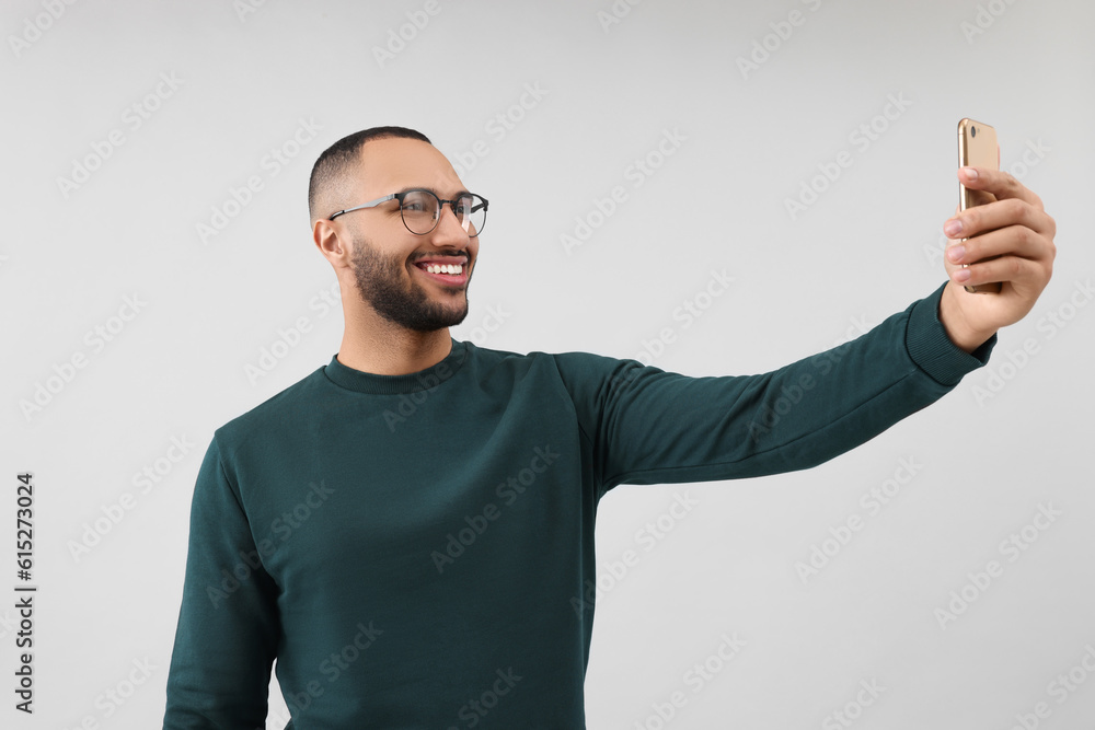 Fototapeta premium Smiling young man taking selfie with smartphone on grey background