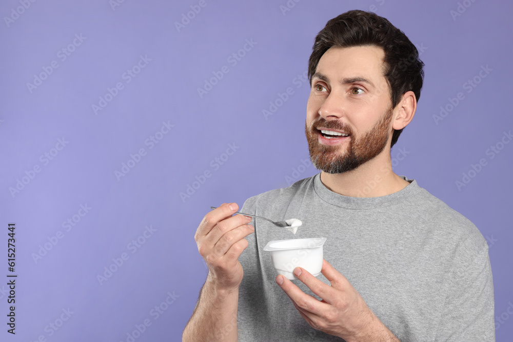 Handsome man with delicious yogurt and spoon on violet background. Space for text Handsome man with delicious yogurt and spoon on violet background. Space for text