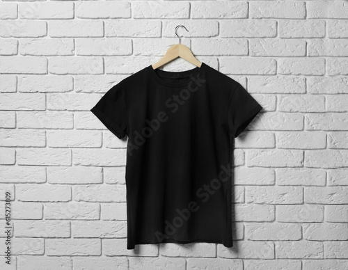 Hanger with stylish black T-shirt on white brick wall