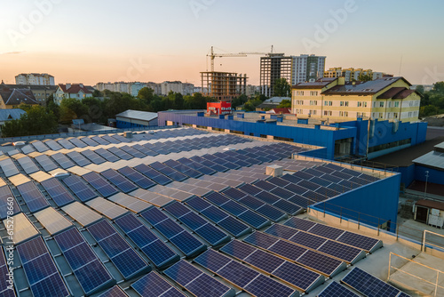 Aerial view of blue photovoltaic solar panels mounted on industrial building roof for producing green ecological electricity at sunset. Production of sustainable energy concept