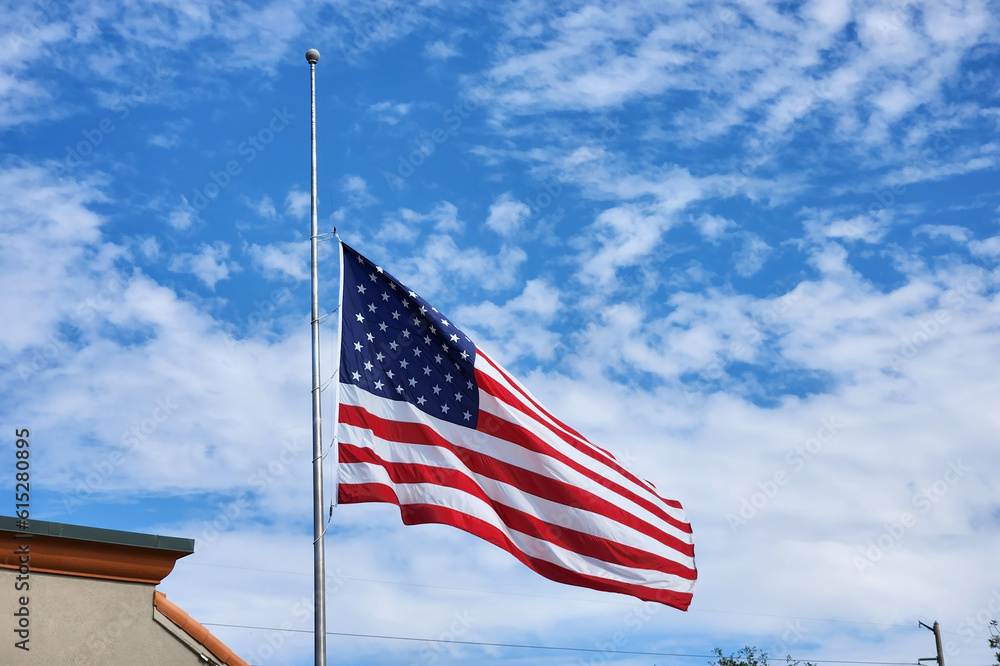 USA national flag waving lowered to half mast on wind against blue sky. American stars and stripes spangled banner as symbol of democracy