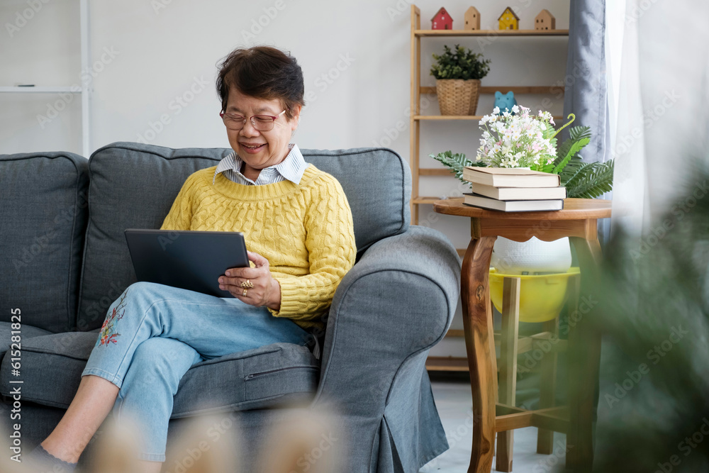 Mature Asian Woman Using Digital Tablet Sitting At Home
