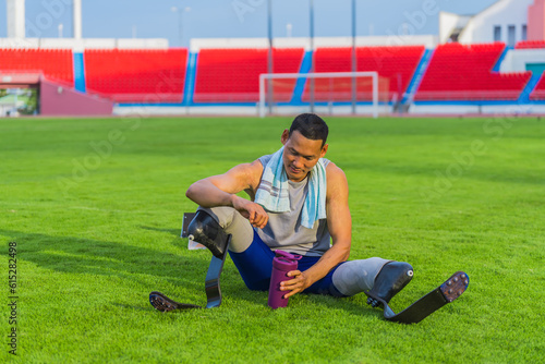 Relaxed Asian Male Athlete with Prosthetic Blades Sitting on Grass Lawn Post Speed-Running Practice at Stadium