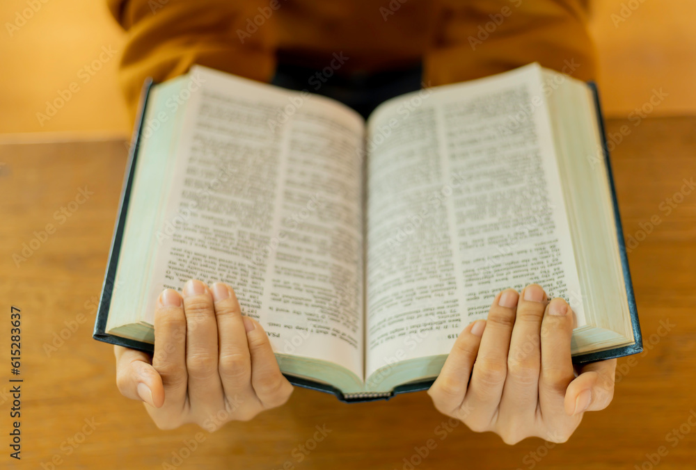 Fototapeta premium Hands holding an open book on a wooden table.