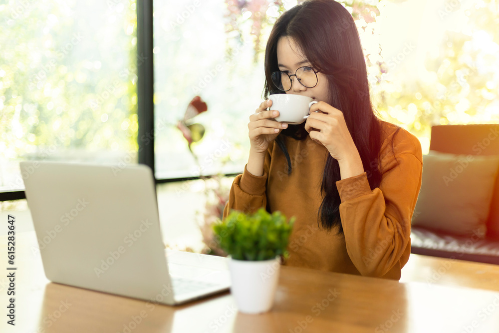 Happy Young Asian woman drinking coffee using Laptop in cafe with sunlight in the morning. Happy Young Asian woman drinking coffee using Laptop in cafe with sunlight in the morning.