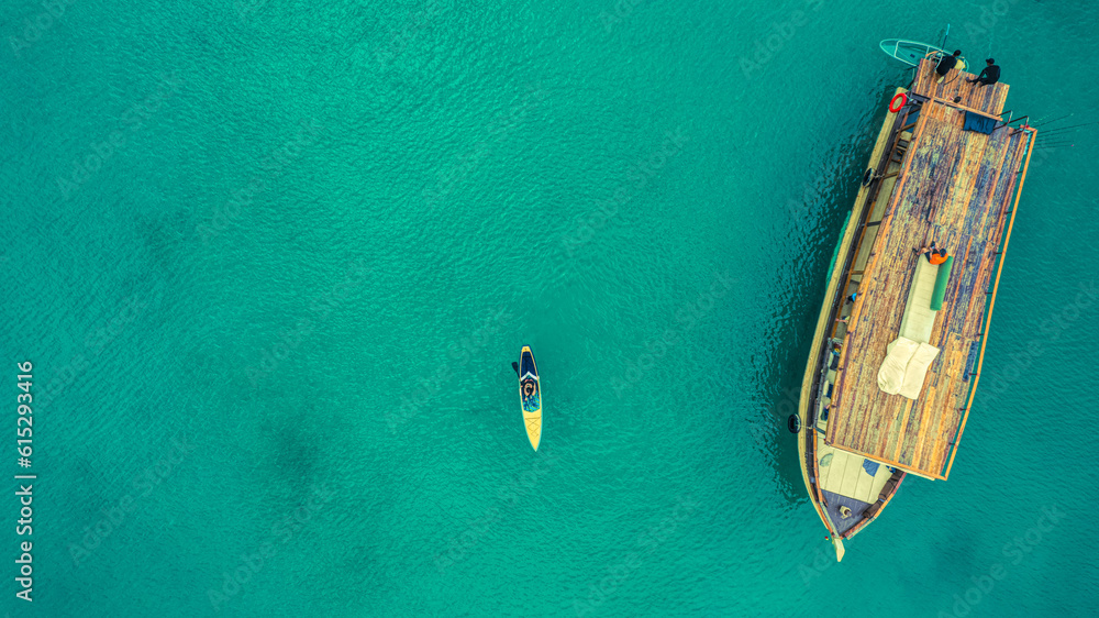 Fishing boat and kayak floating in the sea. The beautiful bright blue water in a clear day.The sun shines the light reflected off the surface. Top view. Fishing boat and kayak floating in the sea. The beautiful bright blue water in a clear day.The sun shines the light reflected off the surface. Top view.